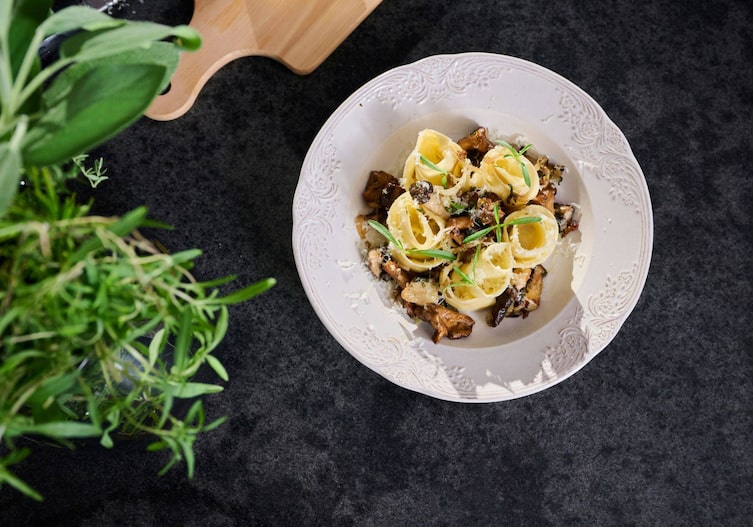 Ein Teller auf schwarzem Hintergrund. Im Teller sind die Pastarosen, gebettet auf gerösteten Waldpilzen.