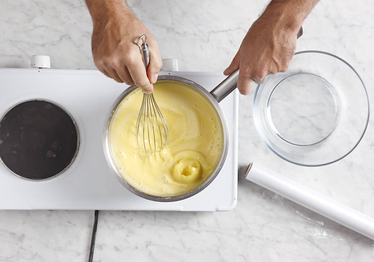 Herdplatte, Glasschüssel, Hände, Schneebesen, Topf, Creme, Frischhaltefolie