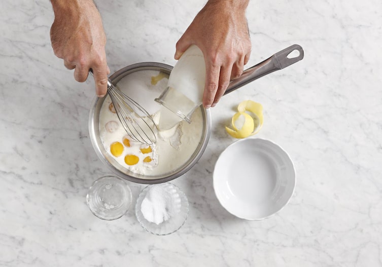 Milch, Dotter, Topf, Zucker, Zitronenschale, Schneebesen, Hände
