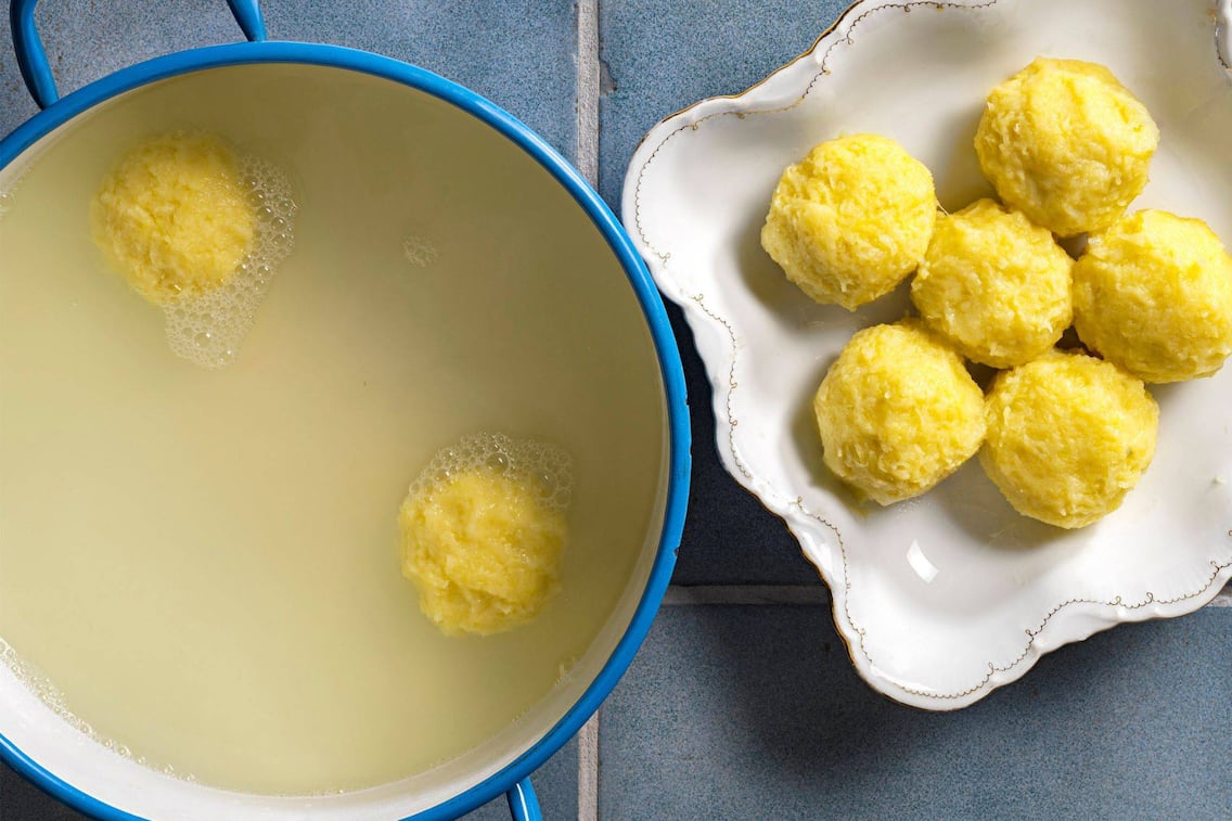 Blauer Email-Kochtopf in dem Kochwasser mit zwei Waldviertler Erdäpfelknödel schwimmen. Daneben steht eine Schüssel mit geschwungenem Goldrand und darin liegen sechs weiter Erdäpfelknödel
