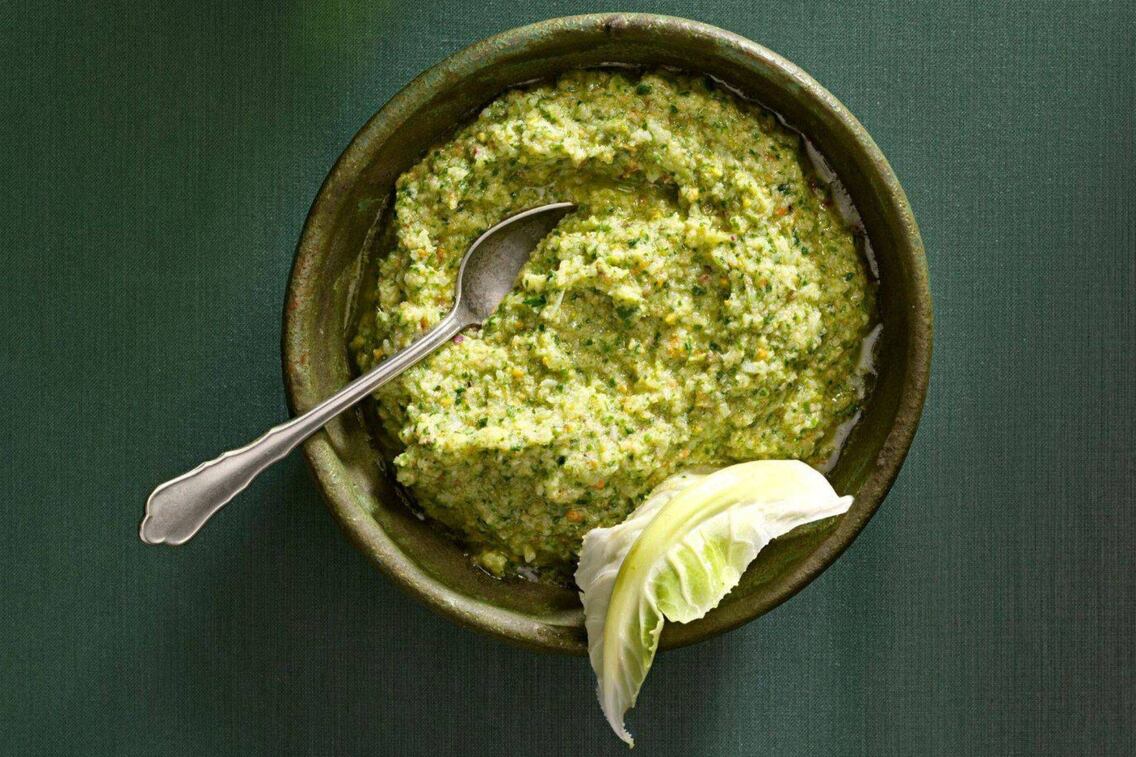 Pesto in einer grüner Keramikschüssel mit einem alten Teelöffel und einem Karfiolblatt