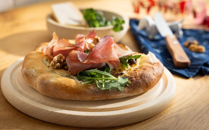 Ein Erdäpfelfladen mit Tiroler Schinkenspeck auf einem Holzbrett