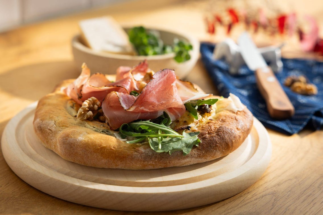 Ein Erdäpfelfladen mit Tiroler Schinkenspeck auf einem Holzbrett