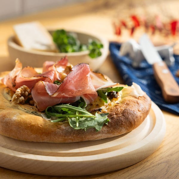 Ein Erdäpfelfladen mit Tiroler Schinkenspeck auf einem Holzbrett