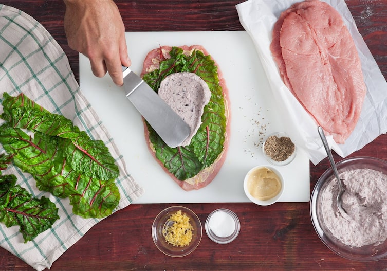 Mangold, Geschirrtuch, Spatel, Kalbsschnitzel, Schüssel, Bohnenpaste, Brett, Löffel, Hand