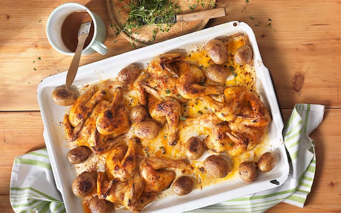 Stubenküken mit Apfelglasur, Küchentuch, Erdäpfel, Kräuter, Holztisch