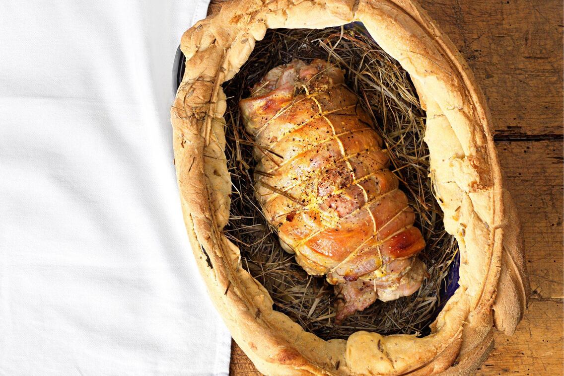 Mit Speck umwickelter und mit einer Schnur geschnürter Lammbraten auf einem Heubett. Der Topfdeckel wurde mit Brotteig am Rand abgedichtet. Der Deckel ist nicht zu sehen.