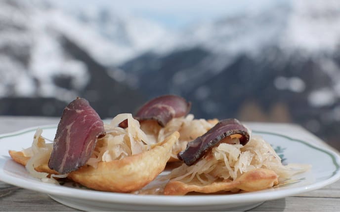 Frittierte Erdäpfelblattl auf einem Teller mit Sauerkraut und einer Scheibe Speck