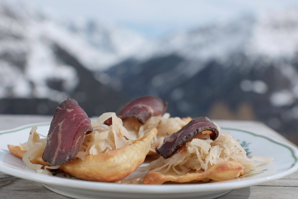 Frittierte Erdäpfelblattl auf einem Teller mit Sauerkraut und einer Scheibe Speck
