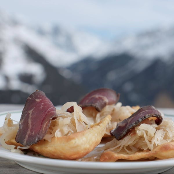 Frittierte Erdäpfelblattl auf einem Teller mit Sauerkraut und einer Scheibe Speck