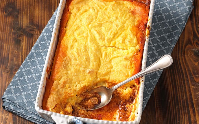 Polenta-Auflauf mit Fleisch und Speck, Holztisch, Löffel, Küchenhandtuch