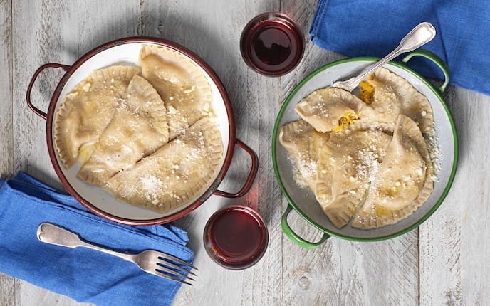 Schlutzkrapfen mit Kürbisfülle, Rotwein, Parmesan, Gabeln, Holztisch, Servietten