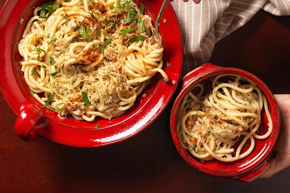 dicke Spaghetti mit Sauerkraut, frisch geschnittenem Petersil und Paprikapulver bestreut, in einer großen und kleinen roten Schüssel angerichet.