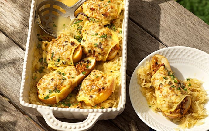 Alter Holztisch von oben fotogfrafiert auf dem eine weiße Keramik-Auflaufform steht mit gefüllten und mit Käse überbackenen Birnen- und Apfelhälften steht. Daneben ist eine Portion mit Sauerkraut auf einem Teller angerichtet.
