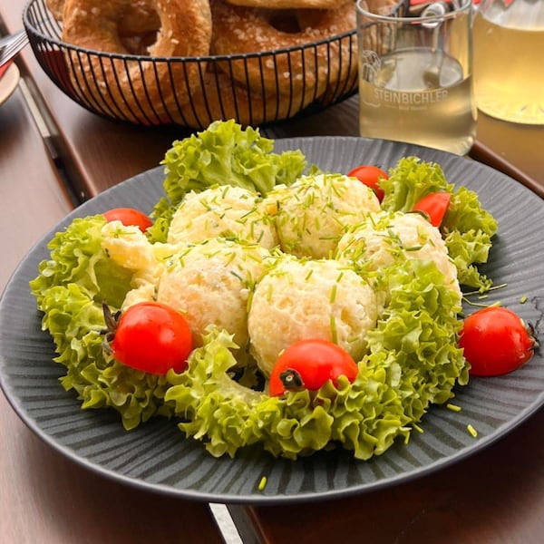 Ostertisch mit Erdäpfelkas, Grünem Salat und Tomatenhälften serviert auf einem dunklen Teller, daneben steht ein Teller mit bunten Ostereiern.