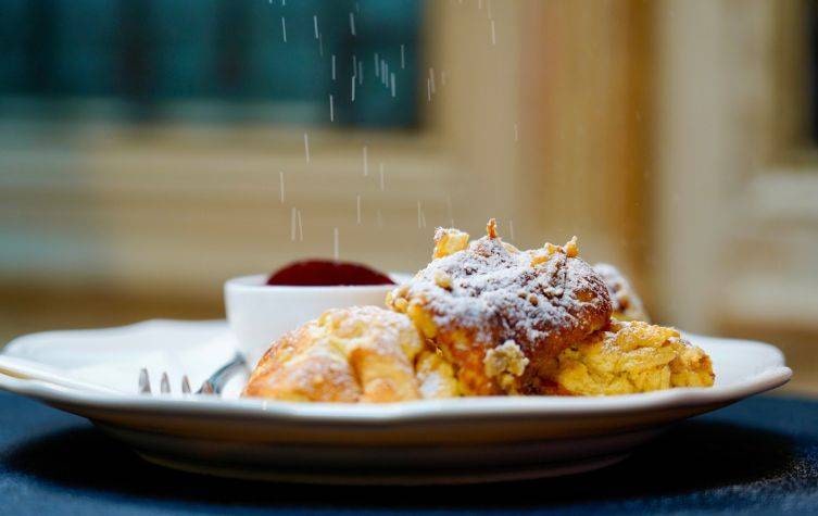 Kaiserschmarrn von Demel in Wien, wie er gerade mit Staubzucker bestreut wird.