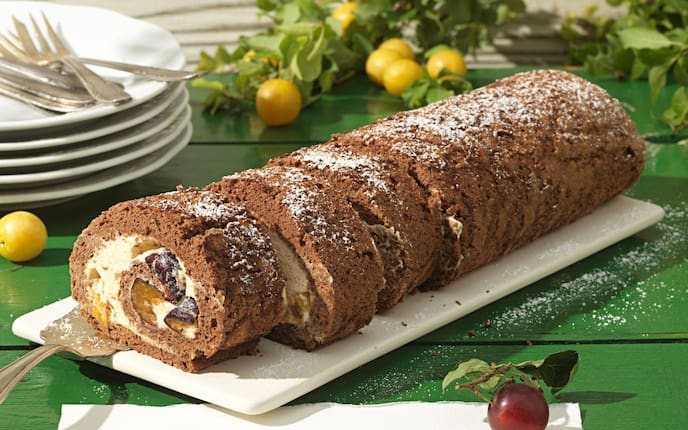 Eine Marzipan-Kakao-Roulade mit Kriecherl als Füllung auf einer weißen Platte serviert.