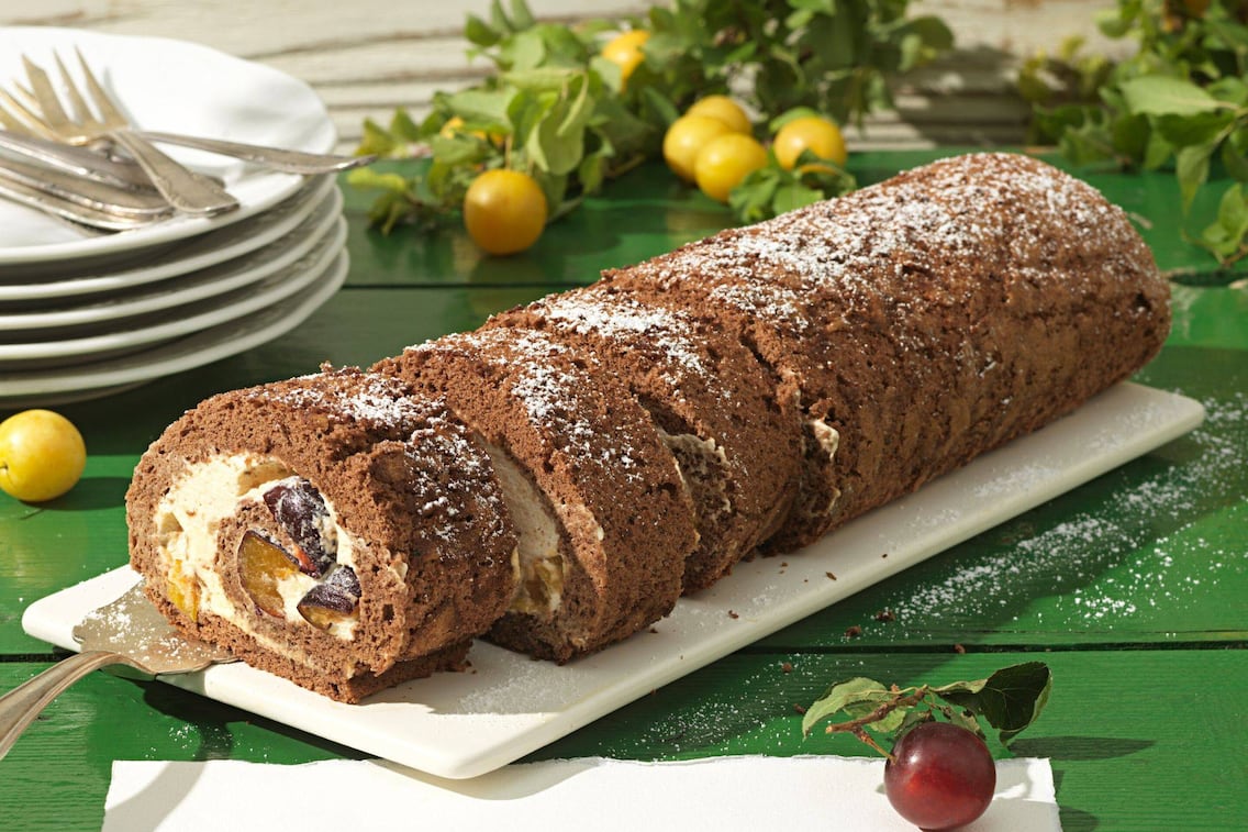 Eine Marzipan-Kakao-Roulade mit Kriecherl als Füllung auf einer weißen Platte serviert.