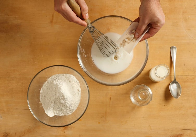 Schüssel, Germ, Schneebesen, Milch, Holztisch