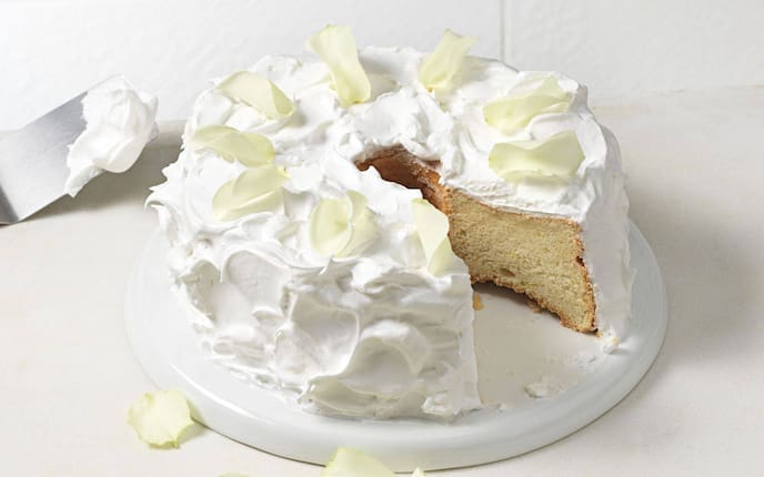 Heller Kuchen mit Baiser umhüllt und Rosenblättern bestreut.