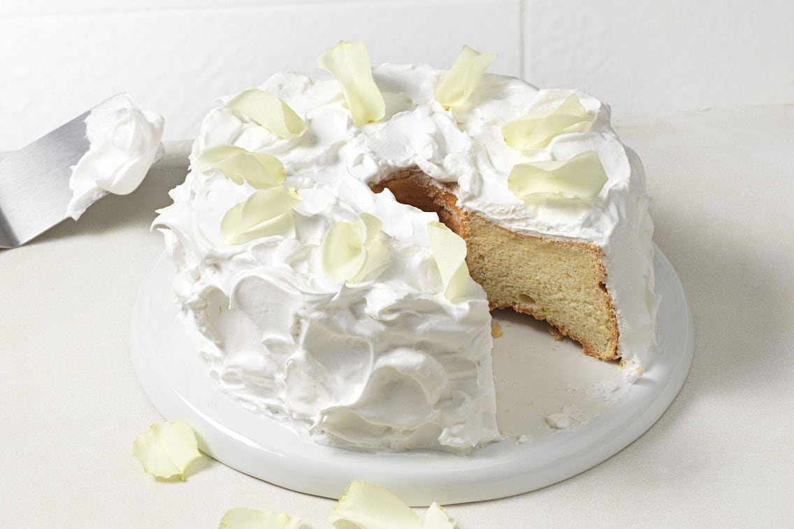 Heller Kuchen mit Baiser umhüllt und Rosenblättern bestreut.