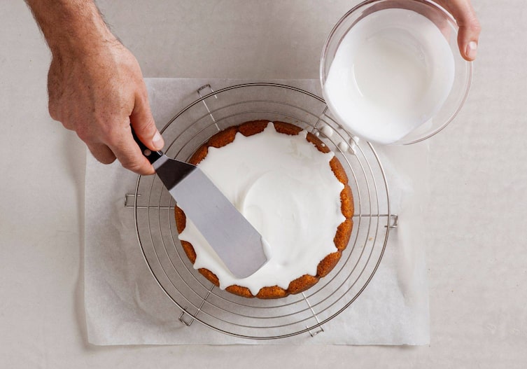 Auf einem Kuchen wird weiße Zuckerglasur geleert und mit einer Tortenspatel verteilt