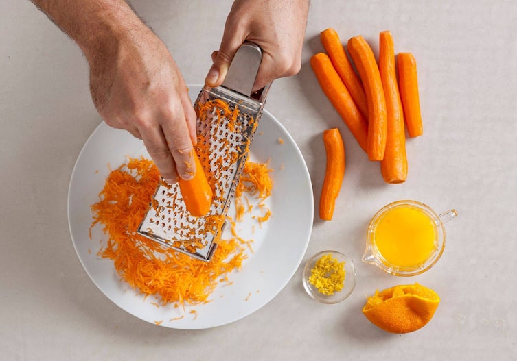 Karotten, die in eine weiße Schüssel mit einer Reibe gerieben werden