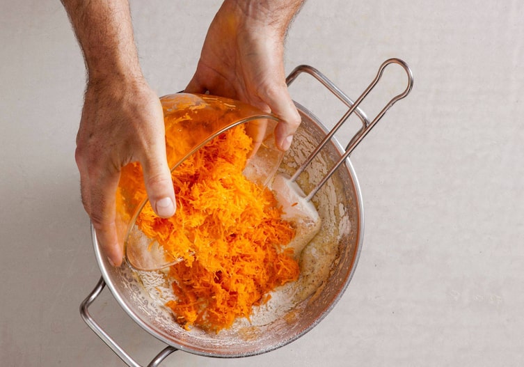 Karottenraspel aus der Glasschüssel werden zum Teig in die Schüssel geleert