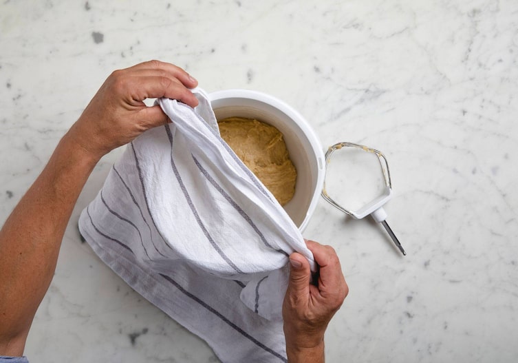 Teigschüssel mit Teig, ein Geschirrtuch wird darüber gelegt.
