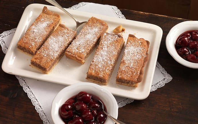 Eichelmehlkuchen mit Rotweinkirschen, Schüsserl, Staubzucker, Kuchenpalette, Tischdecke