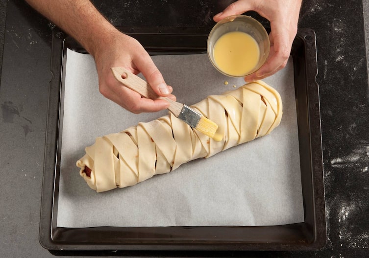 Blätterteigstrudel, Pflaumen, Blätterteig, Dotter, Milch, Pinsel, Hand