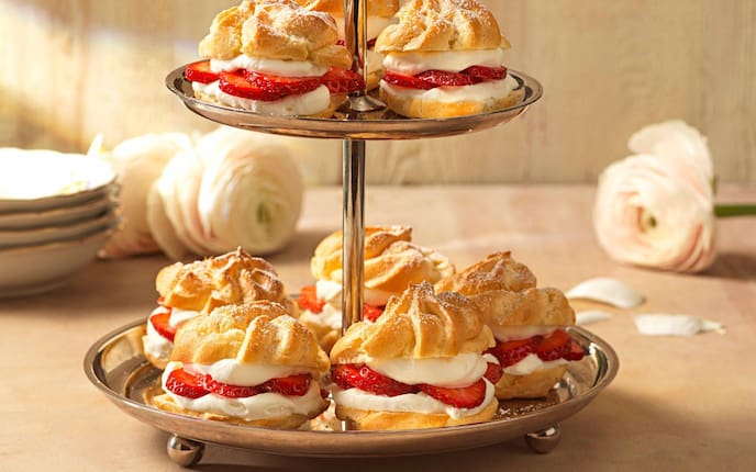 Brandteigkrapferl mit Schlagobers und Erdbeerscheiben gefüllt und auf einer silbernen Etagere fotografiert.