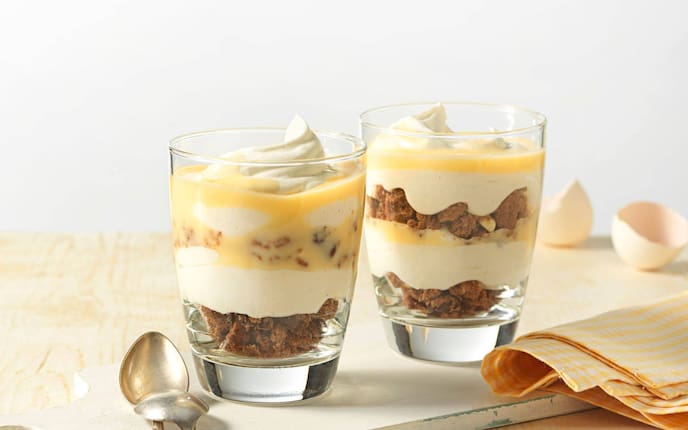 zwei Gläser mit gebrochenen Schokokeksen, Creme, Schlagobers und Eierlikör.