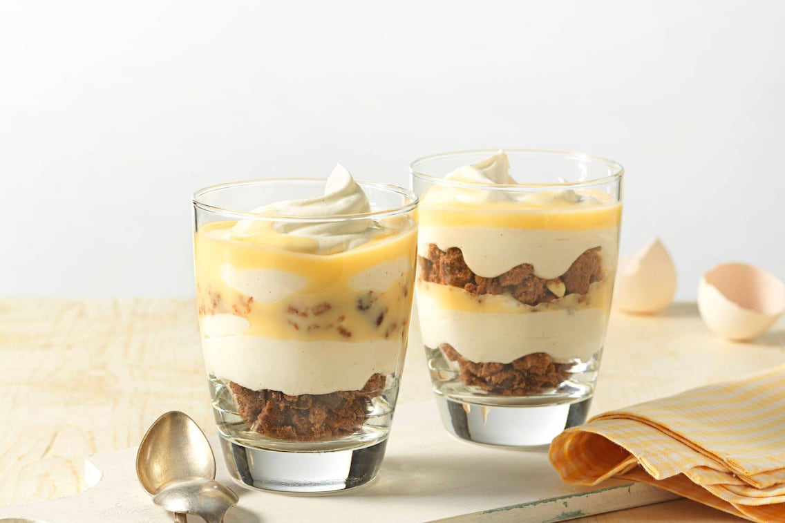 zwei Gläser mit gebrochenen Schokokeksen, Creme, Schlagobers und Eierlikör.