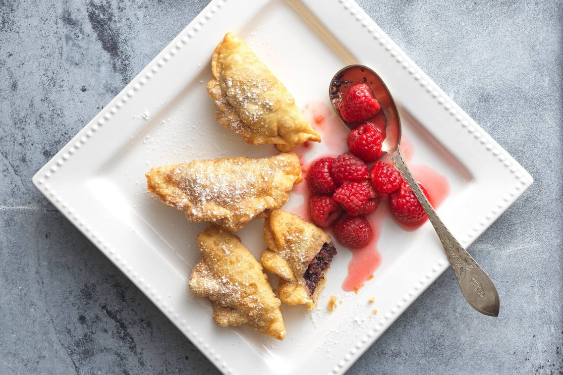 Knusprg gebackene Teigtascherl mit Mohnfülle, angerichtet auf einem viereckigen weißen Teller mit warmen Himbeeren