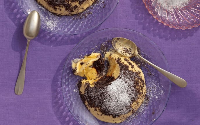 Germköndeleis mit Mohn und Staubzucker auf Desserttellern aus Glas mit Dessertlöfferl. Die Teller stehen auf einer violetten Tischdecke.