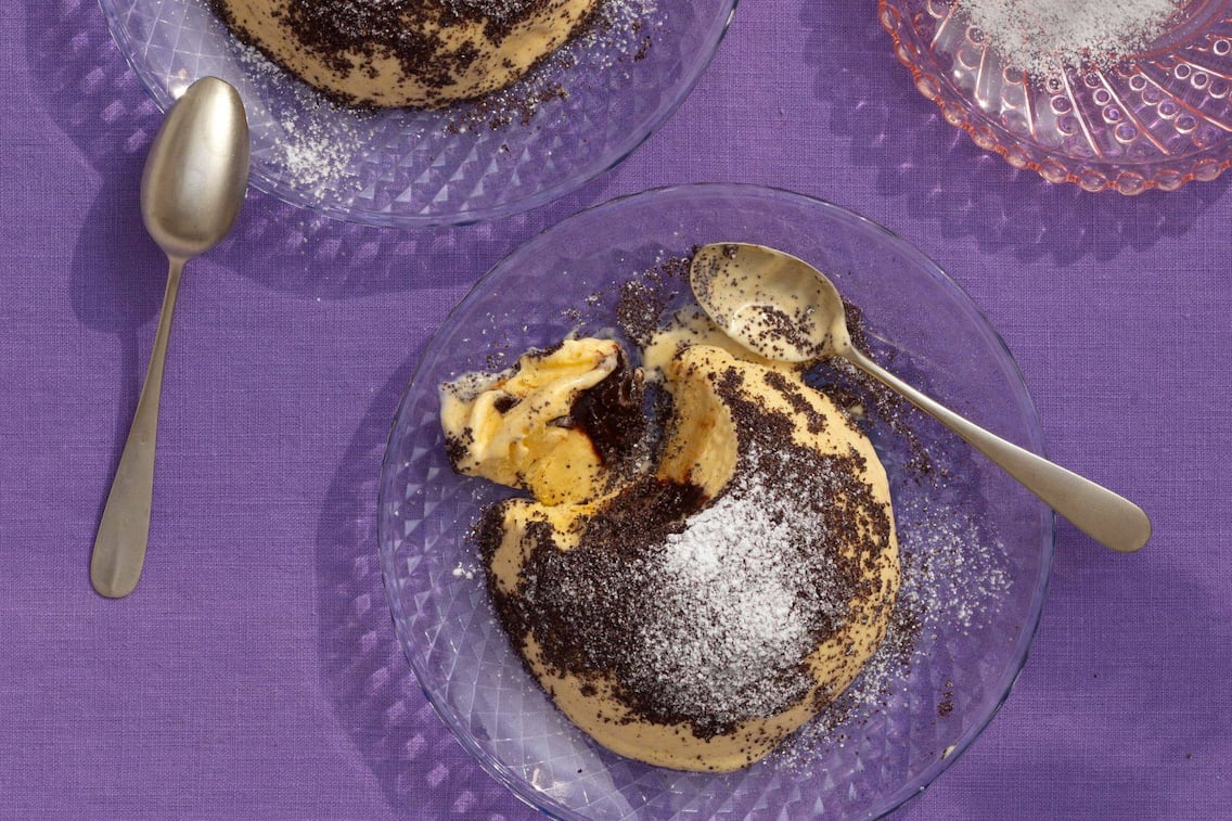 Germköndeleis mit Mohn und Staubzucker auf Desserttellern aus Glas mit Dessertlöfferl. Die Teller stehen auf einer violetten Tischdecke.
