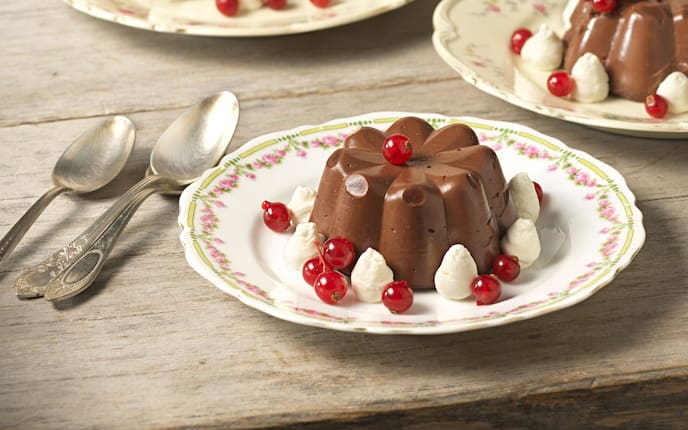 Schokoladenpudding aus dem Förmchen auf einen Teller gestürzt mit Schlagoberstupfer und Ribiseln angerichtet.