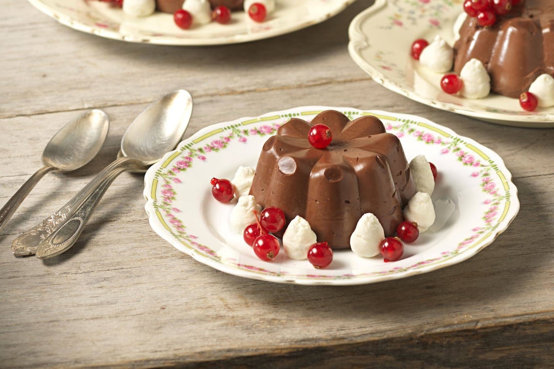Schokoladenpudding aus dem Förmchen auf einen Teller gestürzt mit Schlagoberstupfer und Ribiseln angerichtet.