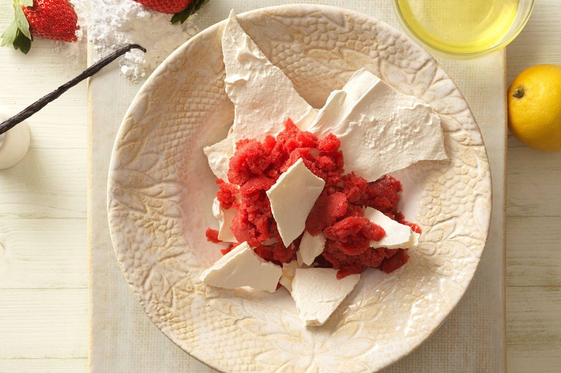 Gebrochenes Baiser mit Erdbeergranité auf einem Dessertteller serviert