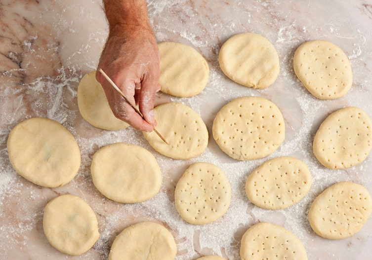 Bemehlte Marmorplatte, auf denen die rohen, gefüllten Teigtaschen liegen. Eine männliche Hand sticht sie mit einem Holzstäbchen mehrmals ein.
