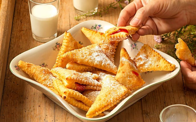 Viele in Schmalz herausgebackene und mit Staubzucker bestreute Polsterzipfe in diner alten Servierschüssel, daneben stehen zwei Gläser Milch