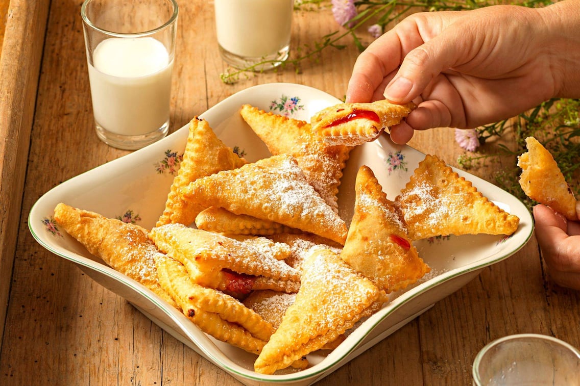 Viele in Schmalz herausgebackene und mit Staubzucker bestreute Polsterzipfe in diner alten Servierschüssel, daneben stehen zwei Gläser Milch