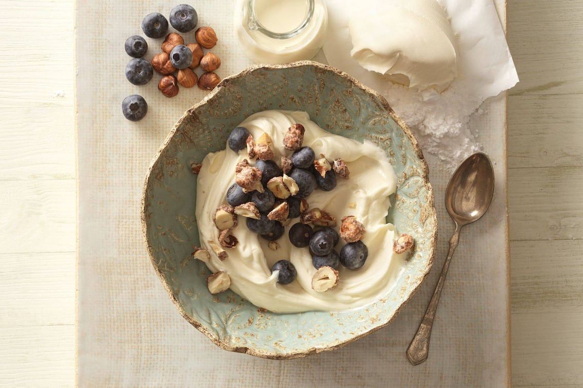 Cremige Mascarponecreme mit karamellisierten Haselnüssen und Heidelbeeren in einer Schale serviert.