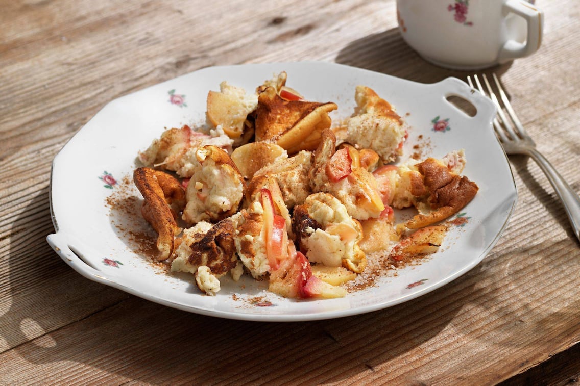 Schmarren mit Afelspalten auf einem Teller mit Blümchen auf einem Holztisch.