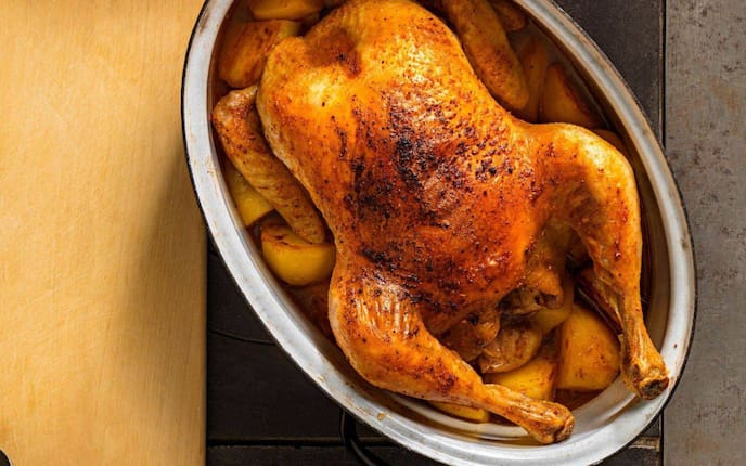 Auf einem alten Tischofen steht ein Bräter mit einem Brathendl und Kartoffel fertig gebraten. Daneben liegt ein Holzbrett mit einem allten kleinen Schöpflöffel