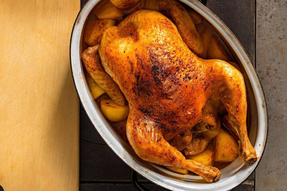Auf einem alten Tischofen steht ein Bräter mit einem Brathendl und Kartoffel fertig gebraten. Daneben liegt ein Holzbrett mit einem allten kleinen Schöpflöffel