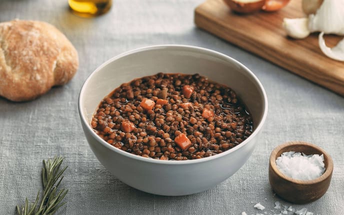 Ziegenkäsebrot gebacken auf Rotweinlinsen, Petersilie, Suppenschale, Holztisch