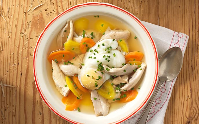 Klare Hendlsuppe mit pochiertem Ei, Hühnerfleisch, Schnittlauch, Löffel, Suppengemüse