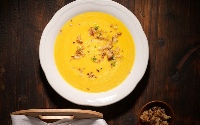 Suppe von Ochsenherz-Karotten, rote Zwiebel, geröstete Walnüsse, Holztisch, Kräuter, Tablett